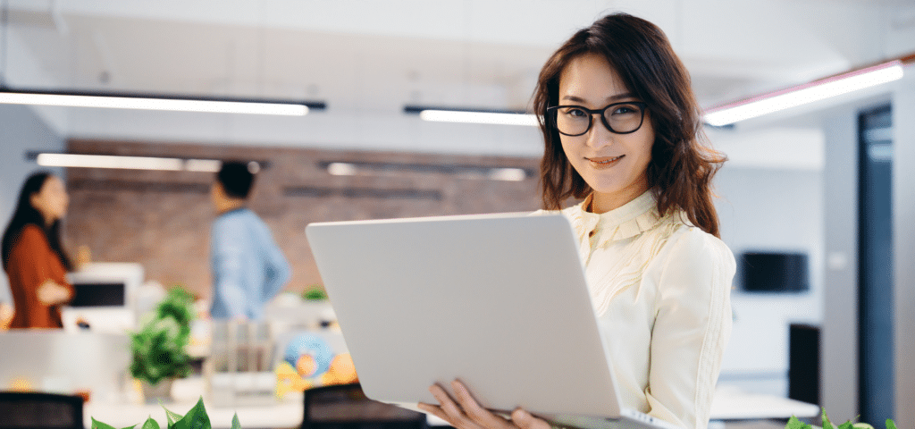 woman in office environment smiling holding a laptop