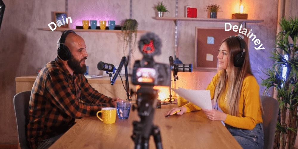 image of male podcast host and female podcast host sitting at a table wearing headsets with microphones in front of them.